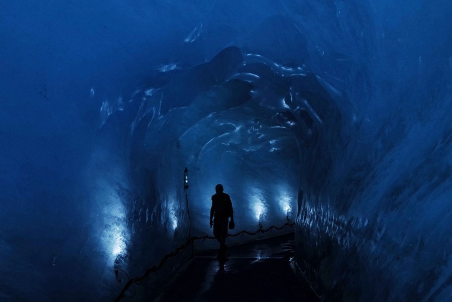 A person walks inside a dark-blue ice cave.