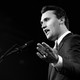 A black-and-white photograph of Charlie Kirk speaking into a microphone.