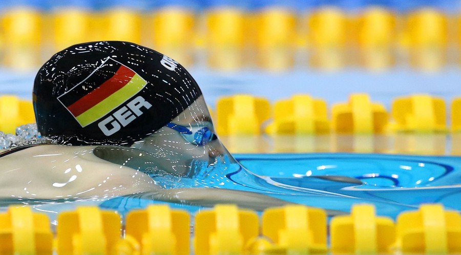 A swimmer is seen in a pool, with water smoothly flowing over their face and head.