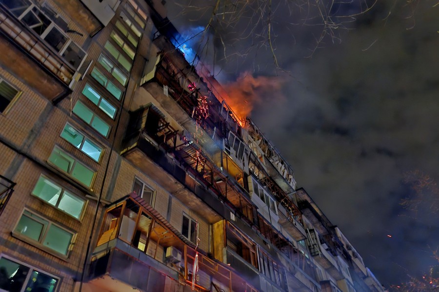 A fire near the top of a nine-story residential building, photographed from the ground