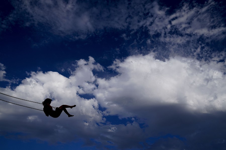 A woman plays on a swing, seen against a partly cloudy sky.