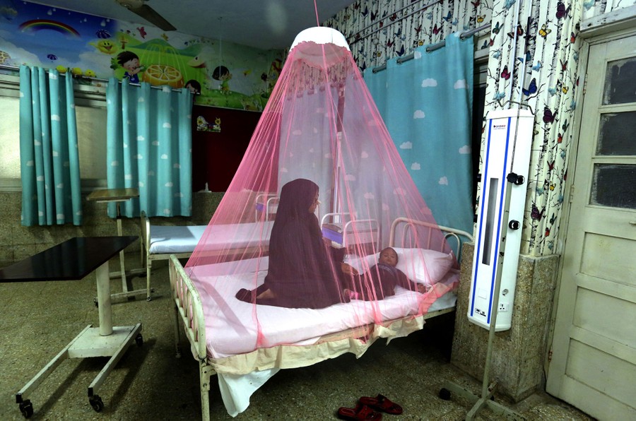 A mother sits on a bed with her young son, under a mosquito net, in a hospital room.