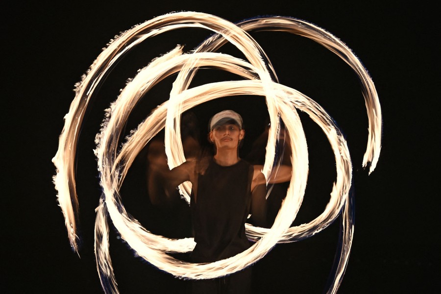 A fire dancer swinging small fireballs around them in multiple arcs captured in a long-exposure image.