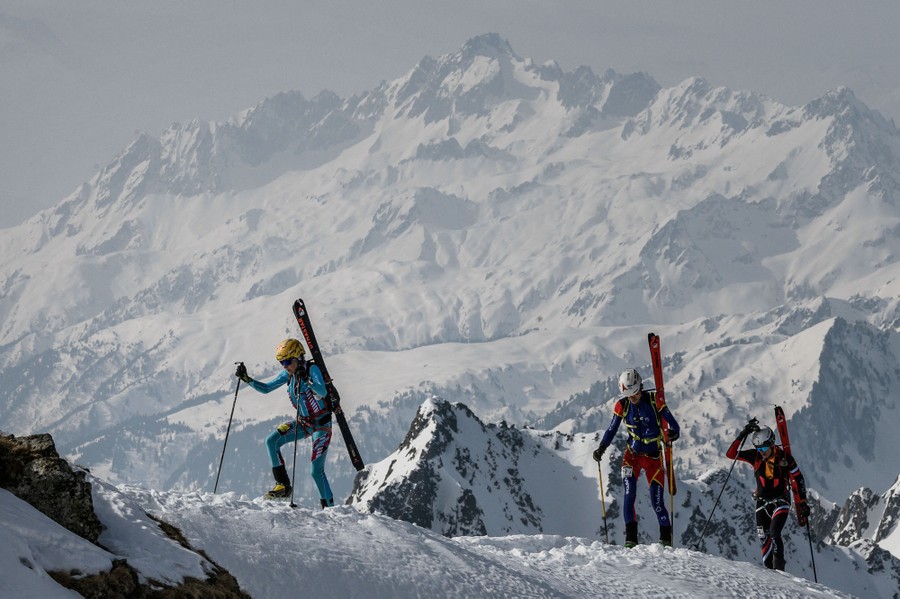Several people carry skis as they hike up a high mountain.