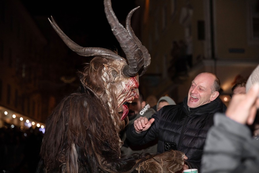 A person in a Krampus costume playfully menaces a smiling person in a crowd.