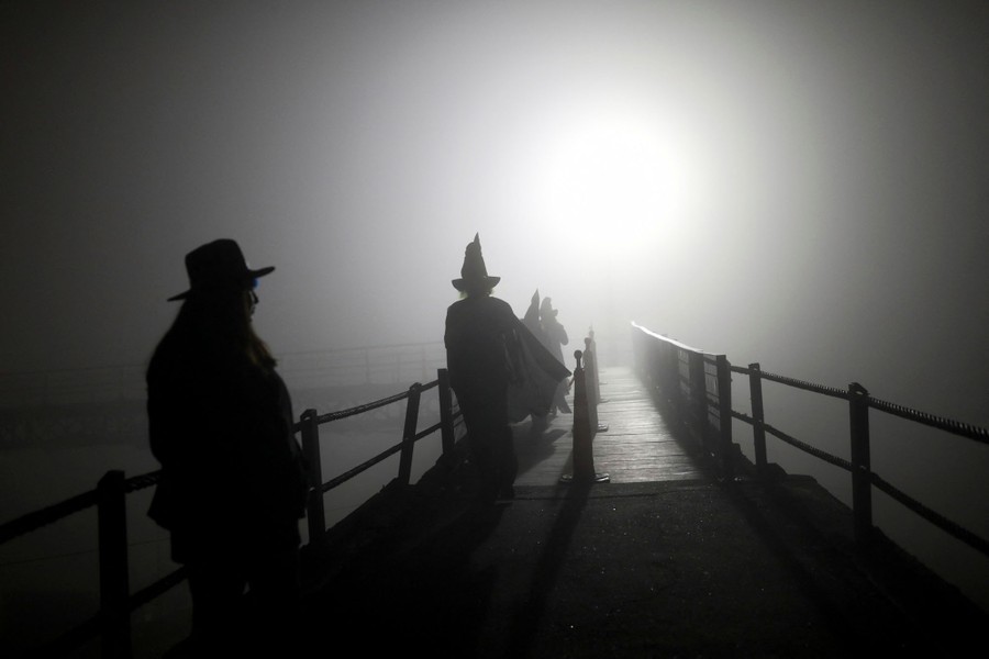 Several people in costume walk toward a light over a footbridge.