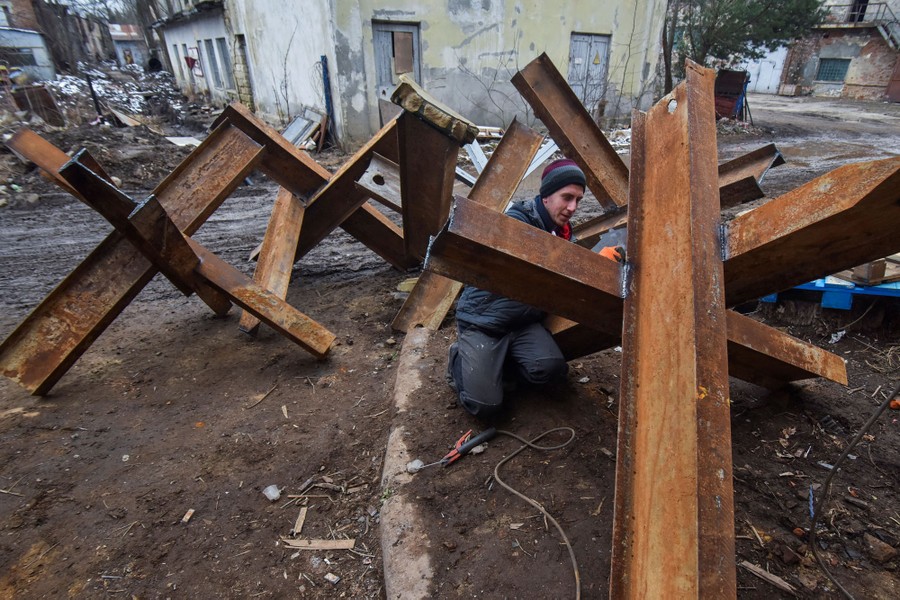 A person welds together chunks of steel beam into a large tank obstacle.
