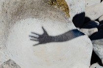 a shadow of someone raising a hand and spreading their fingers apart on a big grey rock