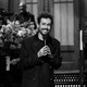 Ramy Youssef smiles on the SNL stage while holding a microphone