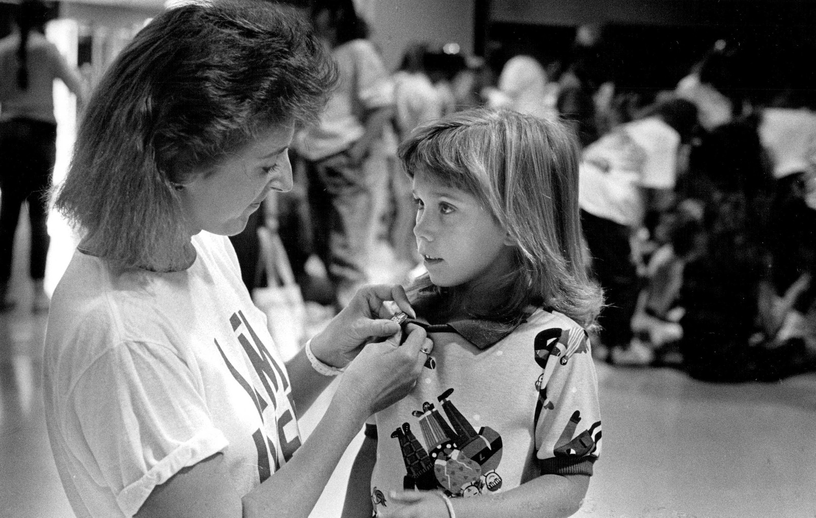 A person kneels down to place a pin on the shirt of a young student.