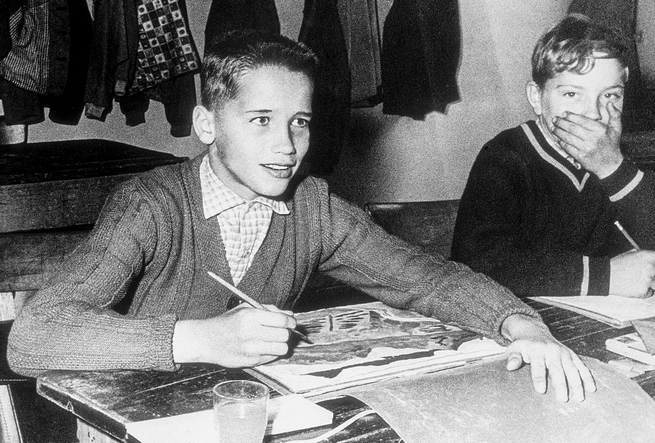 black-and-white photo of boy holding pencil at desk