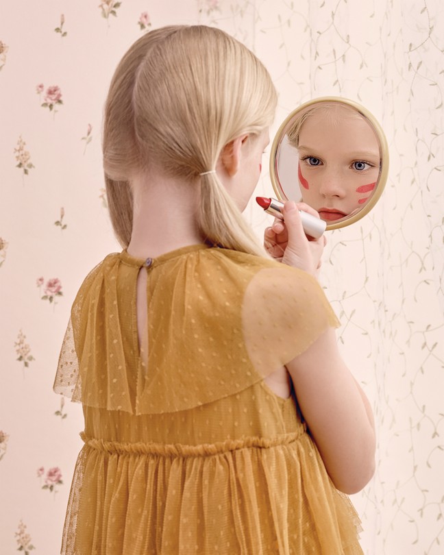 A young girl puts on lipstick in the mirror.
