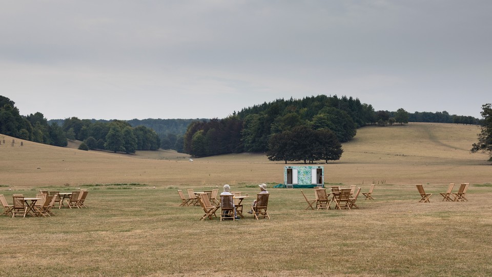Two women sitting in chairs talking to each other in the midst of a wide open field at what looks like a concert venue