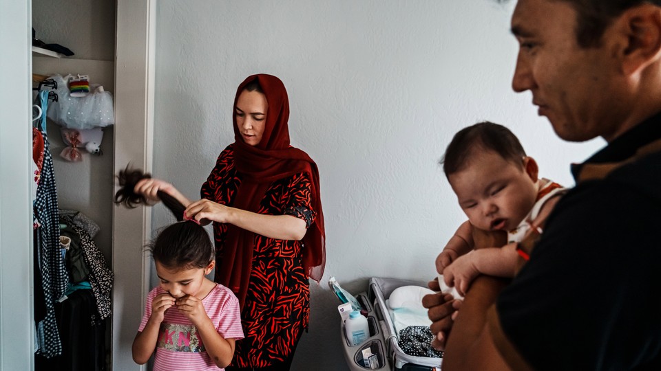A mom ties her daughter's hair into a ponytail while a father holds their son.