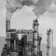 Smoke stacks at an oil refinery are shown against a gray sky