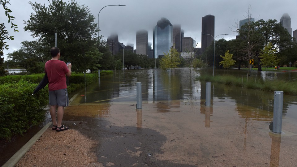 A man stands in a flooded city park, with Houston's skyline in the background
