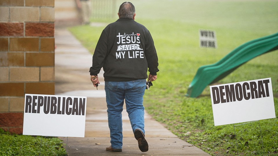 A voter walks past signs at a voting location, wearing a jacket that says, "Jesus saved my life"