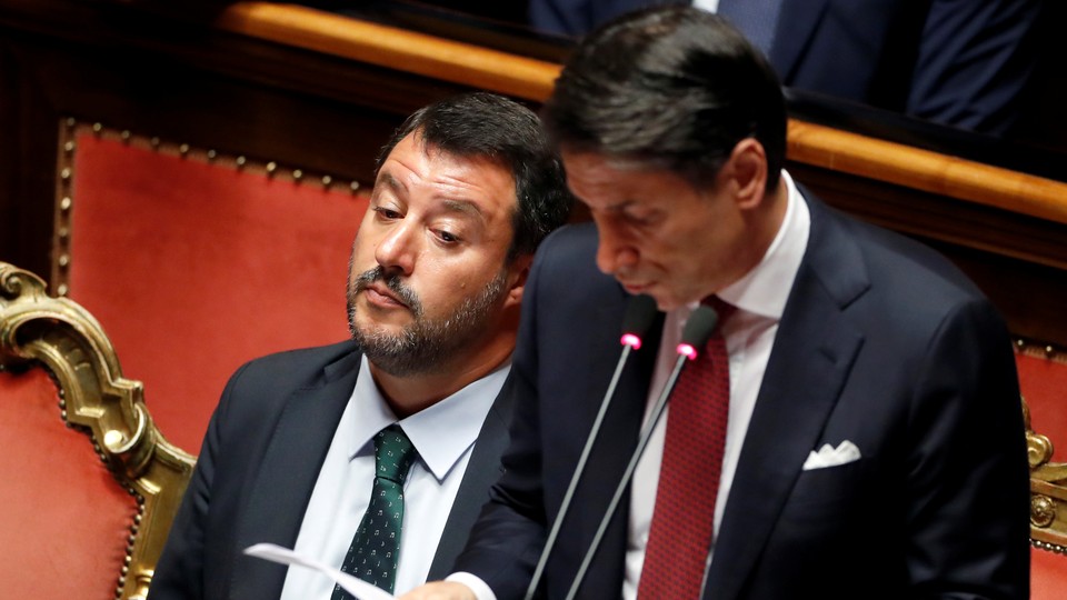 Matteo Salvini stares in dismay as Giuseppe Conte speaks at a podium.