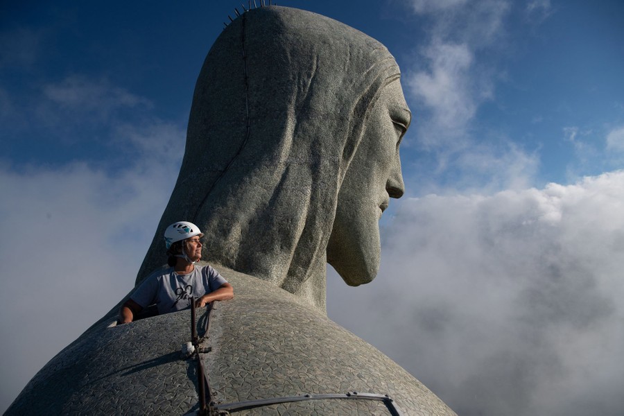 A person peers out from a hole in the shoulder of the large statue of Christ the Redeemer.