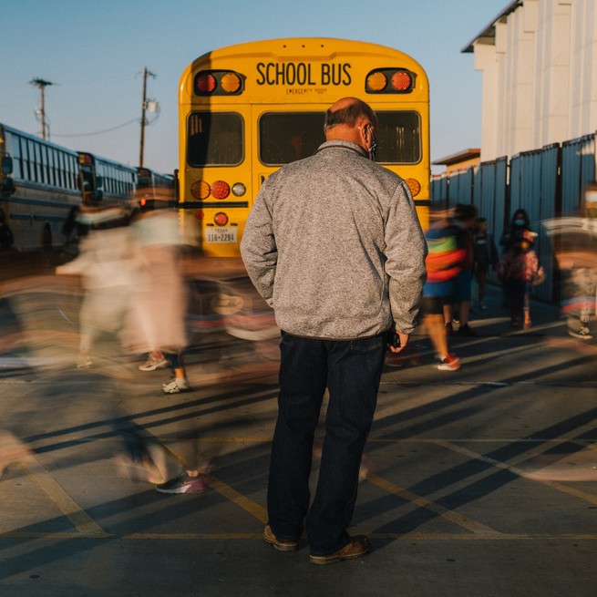 A man wearing a medical mask monitors masked students as they board school buses. 