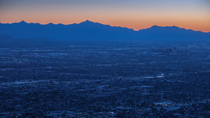 photo of blue-lit urban area at dawn or dusk with blue mountain ridge in background and orange sky