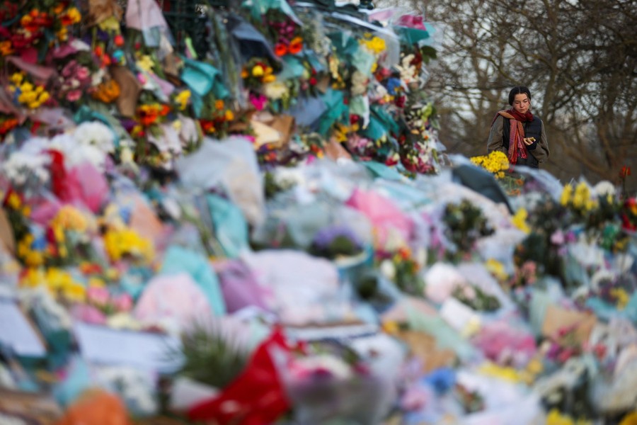 A woman looks at hundreds of bouquets of flowers left at a memorial site.