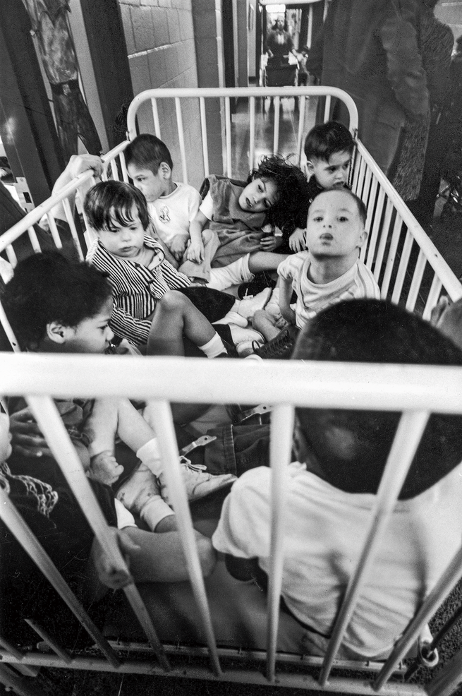 black-and-white photo of a white metal crib full of babies and toddlers
