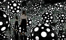A person stands among illuminated spheres in a mirror-walled room.
