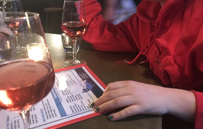 Glasses of wine on a table, a woman wearing a sweatshirt with a tiny sweatshirt sewn onto it.