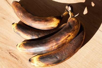 Four very brown bananas laid on their side on a wood surface