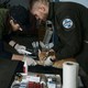 Two people wearing surgical gloves lean over to hold and treat a cat on a table.