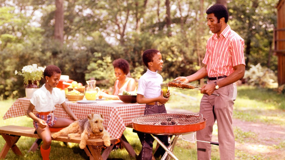 A vintage photo of a Black family sitting around a table and grilling outside
