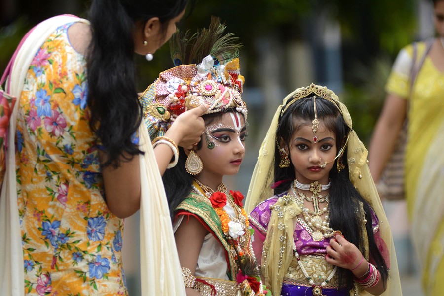 An Indian parent adjusts the costume of her child dressed as Lord Krishna