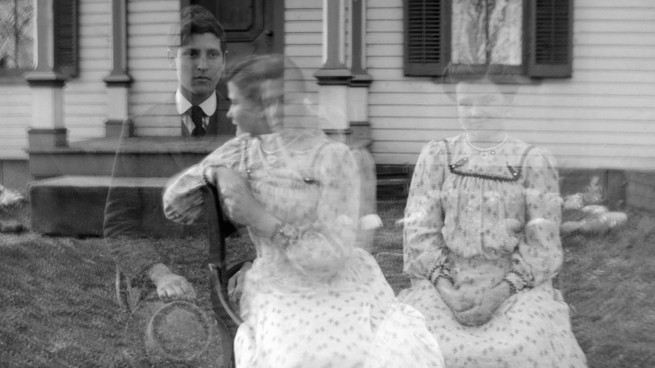 One man and two women in clothes from the past, all semi-transparent like ghosts in front of a house's porch