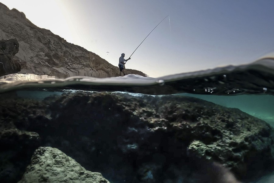 An over-under view of a fisherman on a shore, and a glimpse under the water.