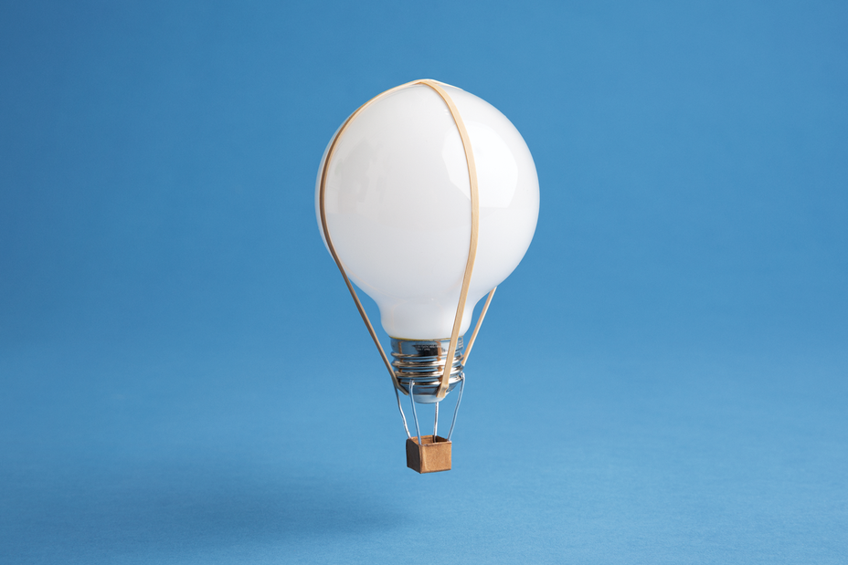light bulb with basket suspended below it to look like a hot-air balloon on blue background