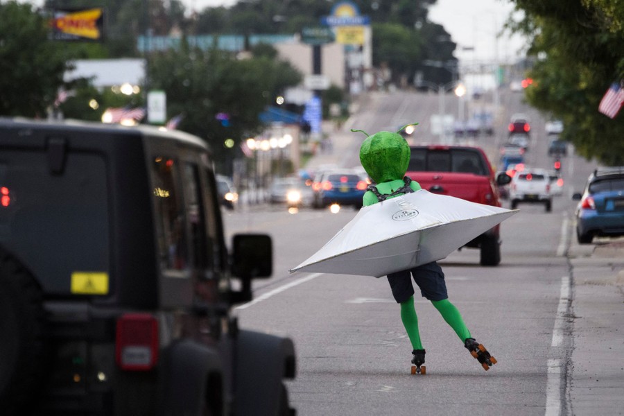 A person wearing an alien costume in a flying saucer roller skates through traffic.