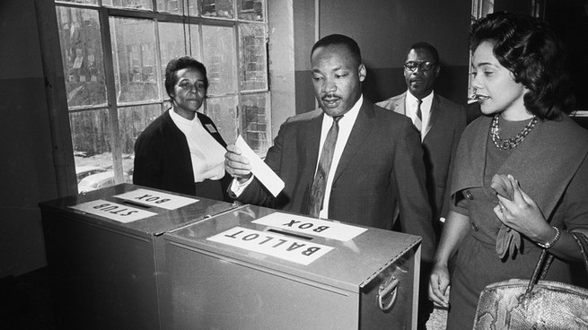 King casts his ballot in Atlanta in 1964, while his wife, Coretta, waits.