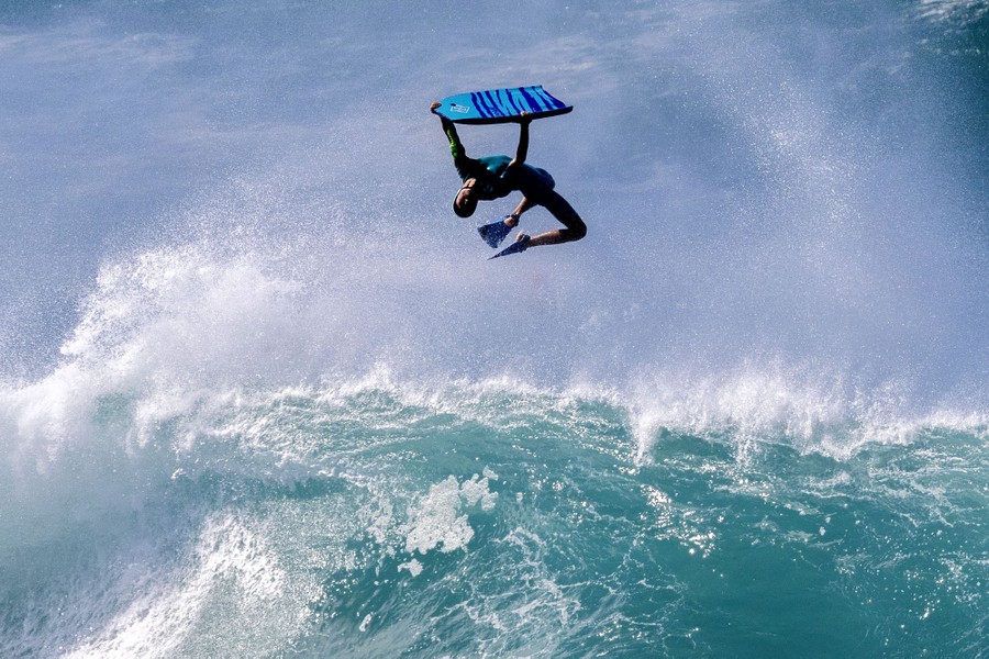 A bodyboarder tumbles in the air above a wave.