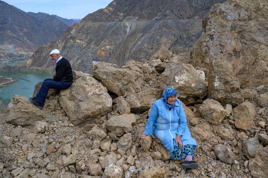 Two people sit on a rocky outcrop, looking down at a valley that is being flooded.