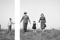 A black and white image of a family holding hands on a hill, with a gap between the son's hand and the father's