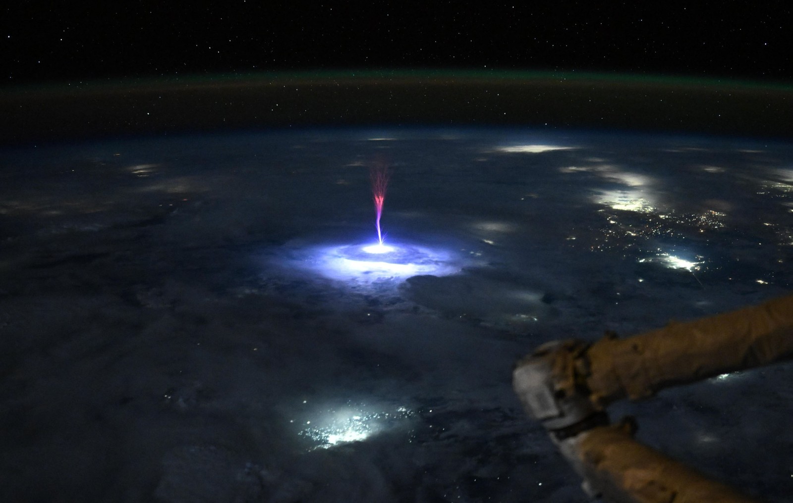 A nighttime view of the Earth, from orbit, with a bright blue-and-red bolt of electrical energy shooting up from a lightning strike in a storm below