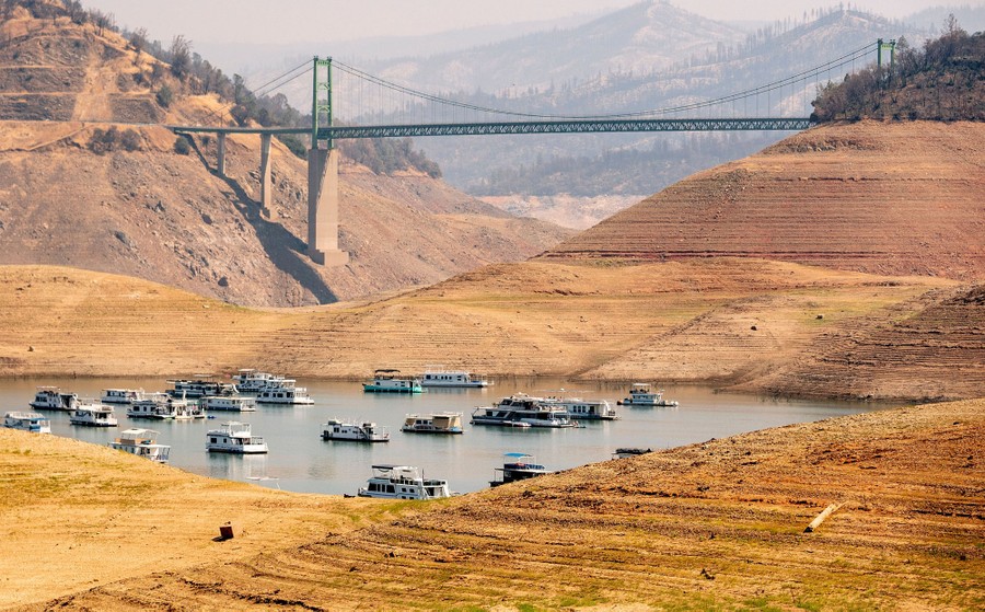 Houseboats sit in a shrinking body of water at the bottom of a ravine—a drying reservoir.