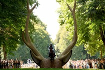 A horse and rider leap over a hurdle shaped like the head of a large stag with very tall antlers on each side.