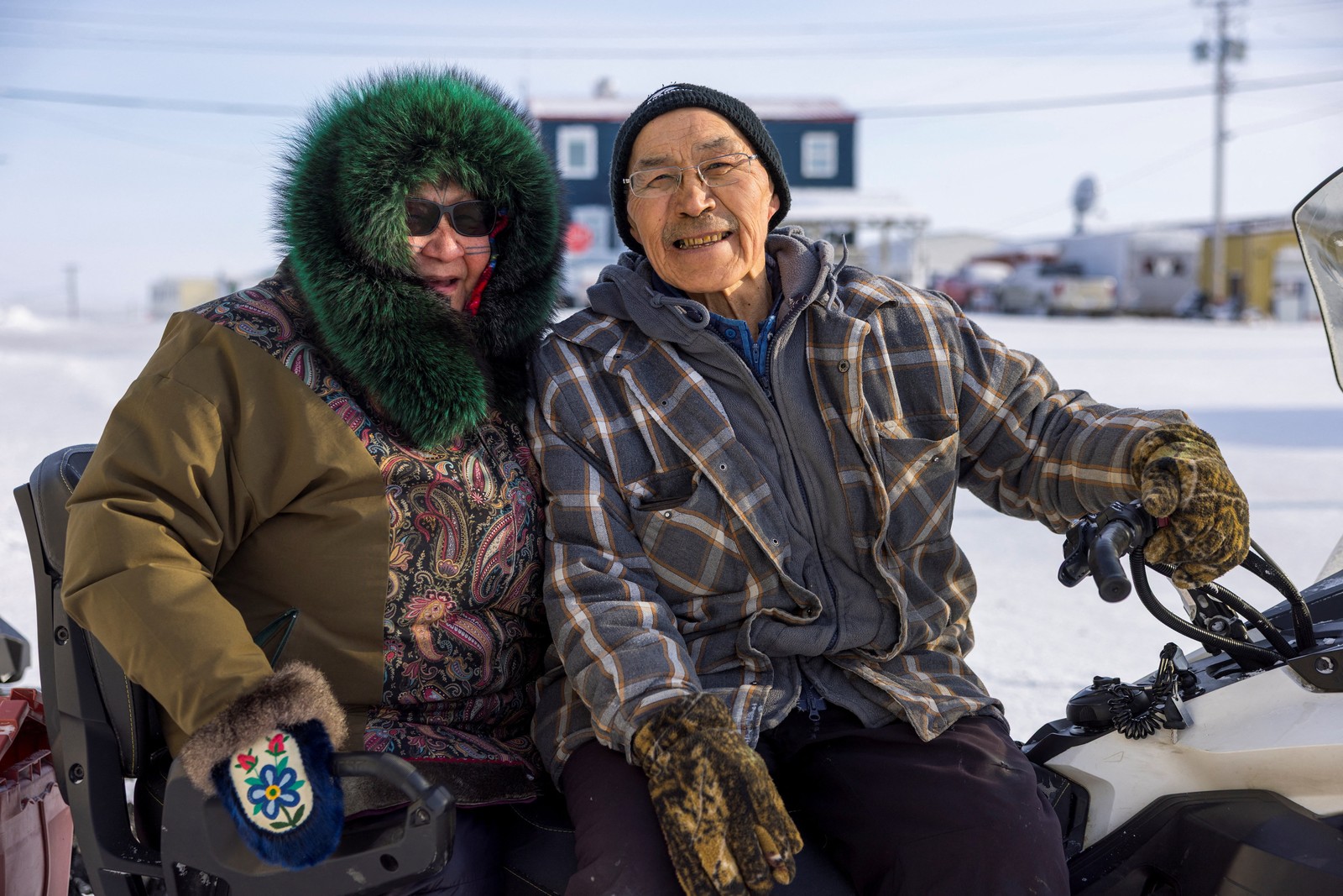A couple dressed in warm clothing smile and pose for a photo while sitting on a snowmobile.