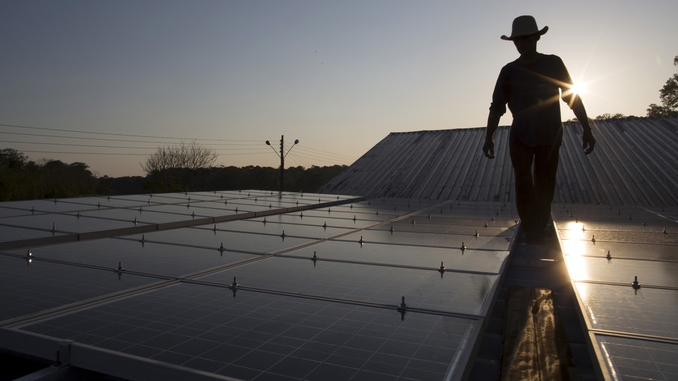 A person wearing a cowboy hat walks along a row of solar panels.