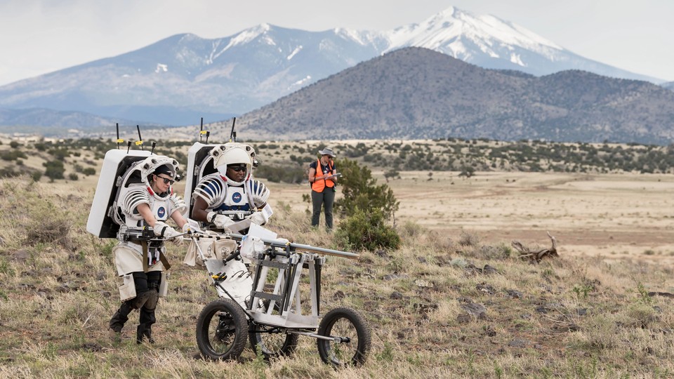 NASA astronauts push a tool cart loaded with lunar tools through the San Francisco Volcanic Field north of Flagstaff, Arizona, as they practice moonwalking operations for Artemis III.