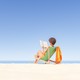 A woman sits on the beach reading a book