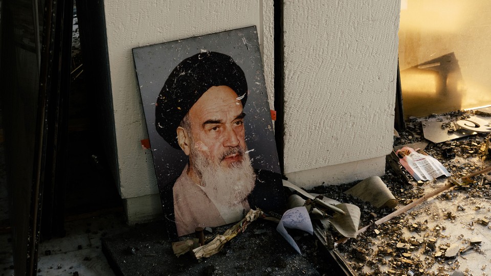 A portrait of Ayatollah Khomeini leaning against a white wall amid rubble and debris