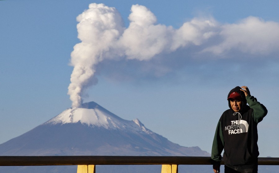 A man walks, with an erupting volcano seen in the background.